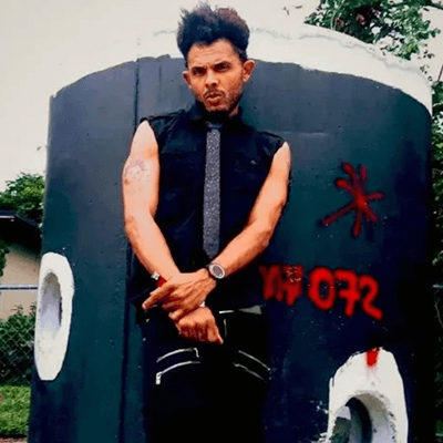 Back of a man at a concert. Hes wearing a beanie hat and a baggy denim jacket with studs. Photo with a purple hue